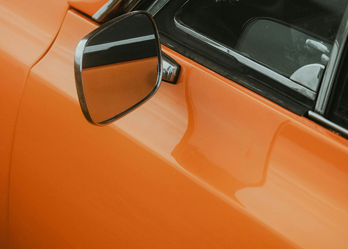Close-up of a vintage orange car's side mirror reflecting the window, illustrating a story about horrible gifts received.