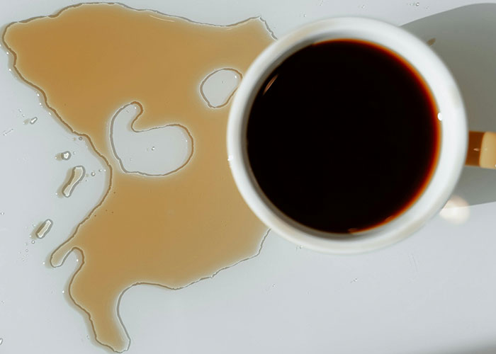 Top view of spilled coffee next to a cup on a white surface illustrating people sharing life hacks for daily use.