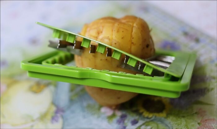 Green vegetable slicer cutting a potato, illustrating sharp knives as a common home cooking mistake.