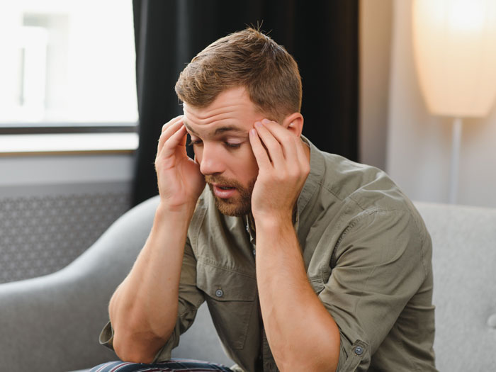 Stressed young man holding his head indoors, illustrating entitled parents ignoring autistic brother's troubling behavior.