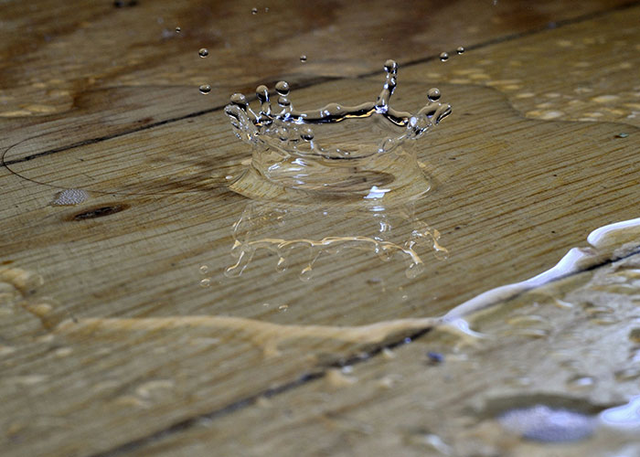 Close-up of water splash on wooden surface, illustrating a cleaning hack inspired by laziness and practical genius.