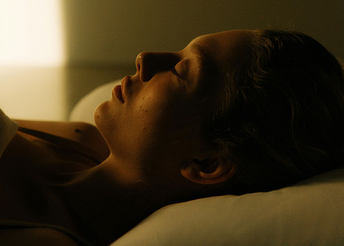 Woman lying in bed with eyes closed in dim light, conveying a sense of eerie or bizarre events creeping people out.