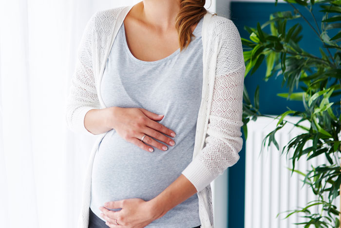 Pregnant woman gently holding her belly indoors, illustrating themes of family drama and personal stories.