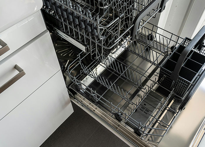 Open dishwasher with empty racks inside a modern kitchen, illustrating genius cleaning hacks inspired by laziness.
