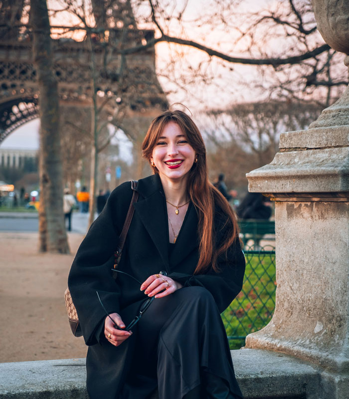 Young woman smiling near the Eiffel Tower, capturing an Oscar-worthy performance moment in a relaxed outdoor setting.