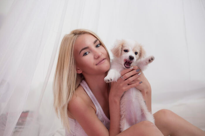 Young woman holding a small white puppy indoors, showing playful and loving moments of an insane dog mom.