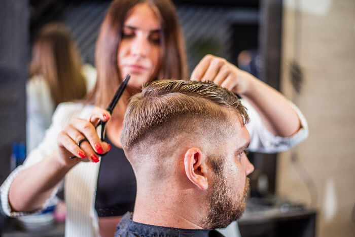Dad getting a haircut by a woman hairstylist, one of the lovable clueless dads doing things during pregnancy.