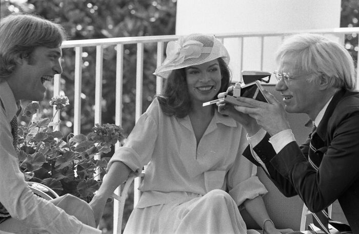 Three style icons in vintage fashion, smiling and interacting with a camera on a sunny outdoor terrace.