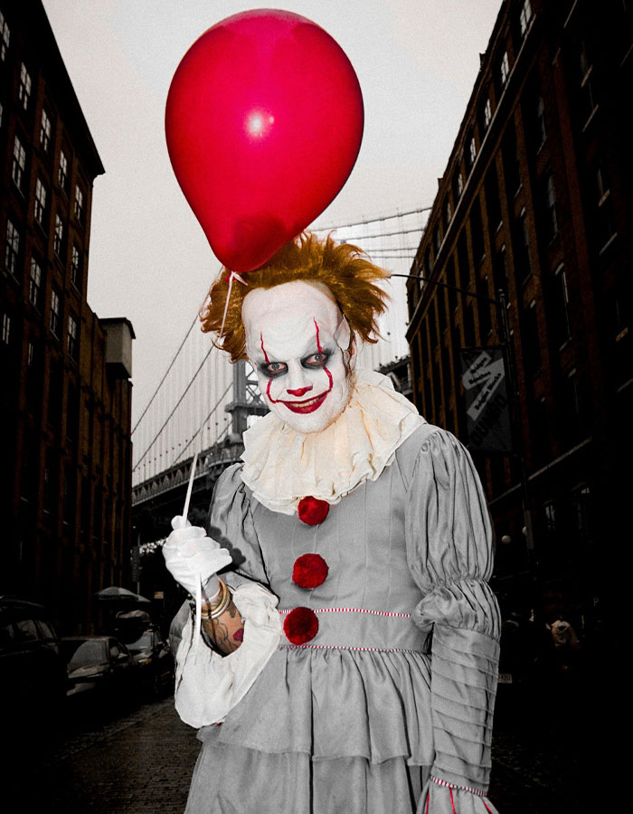 Person dressed as a creepy clown holding a red balloon, showcasing one of the best Halloween costumes by celebrities this year.