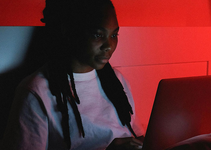Person in a dimly lit room with red light, focused on a laptop, representing terrifying things found online.