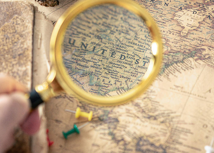 Magnifying glass highlighting a vintage map near push pins, symbolizing fascinating items found in the walls of homes.