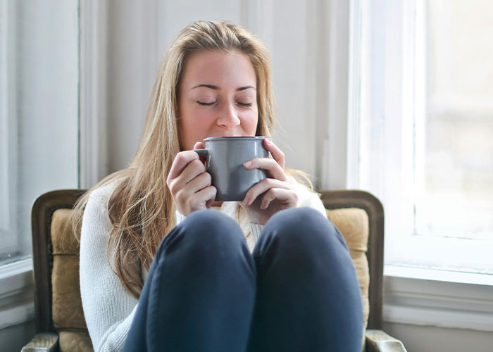 Woman enjoying a warm drink while sitting by the window, illustrating life hacks people can't believe others don't use.