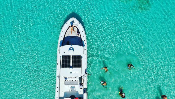 Aerial view of a boat in clear turquoise water with men swimming nearby, related to arrest over foreign island plan.