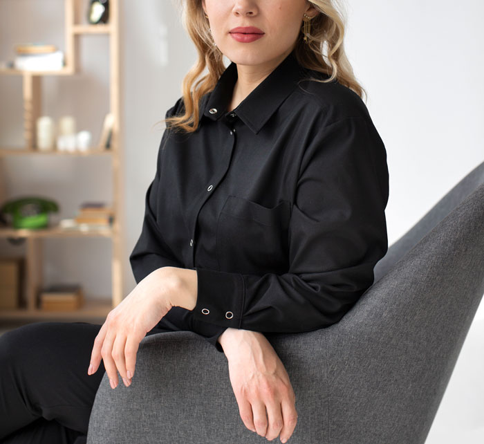 Young woman in a black shirt sitting thoughtfully in a gray chair, reflecting on wild family drama shared online.