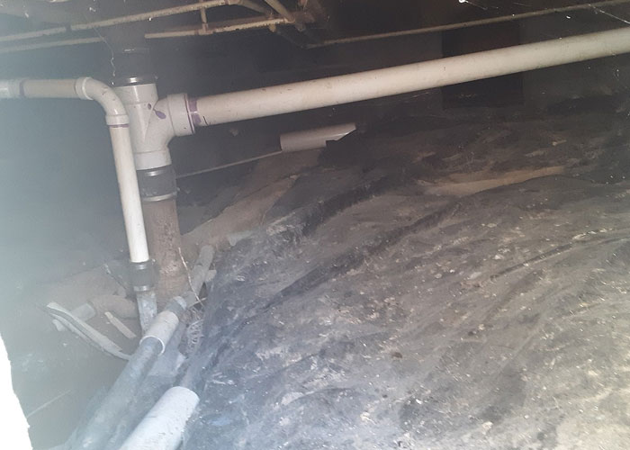 Crawl space under a home showing plumbing pipes and a hidden object partially covered by dirt and debris in the walls.