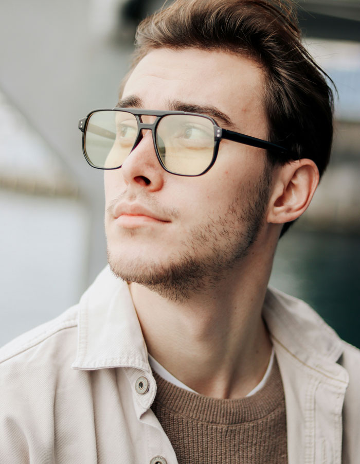 Young man wearing glasses and a beige jacket looking away, embodying an Oscar-worthy performance in a candid moment.
