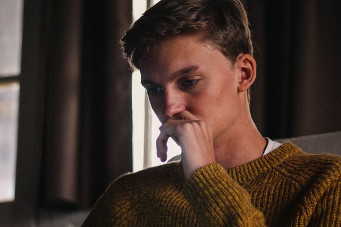 Young man in a yellow sweater appearing anxious and picking at his food during dinner with mom’s boss. Young man in a yellow sweater appearing anxious and picking at his food during dinner with mom’s boss.