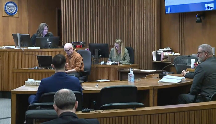 Courtroom scene showing legal professionals and a defendant during a hearing about a dad leaving 2YO in hot car case.