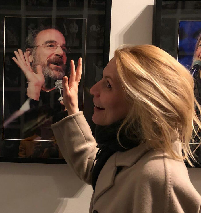 Claire Danes smiling and touching a glass frame, showcasing her quivering chin in a candid moment indoors.