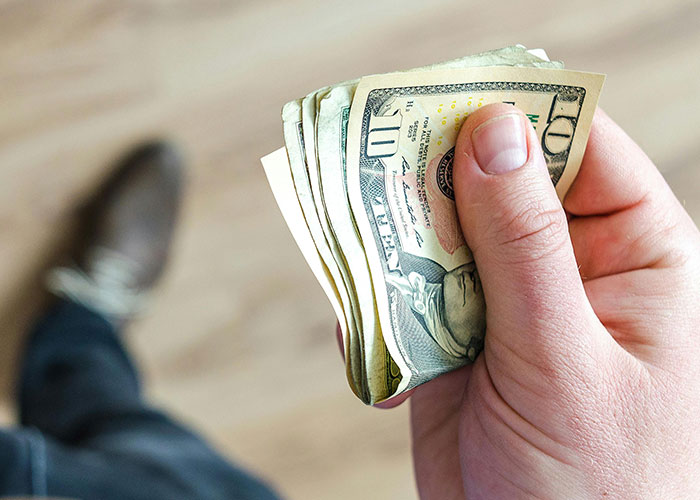 Close-up of a person holding a folded stack of US dollar bills, illustrating common knowledge about money.