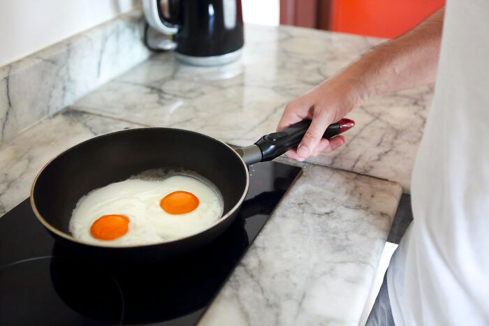 Person cooking two fried eggs on a stovetop in a kitchen, illustrating most insane dog mom things humor.