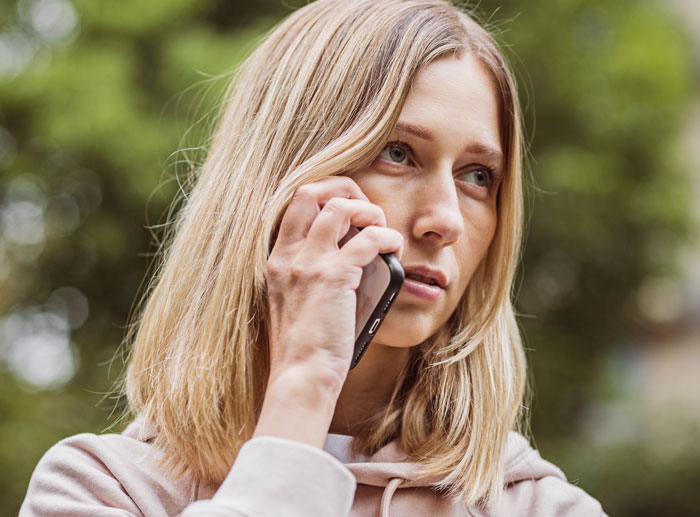 Young woman with blonde hair talking on a phone outdoors, looking concerned and reflective, representing entitled MIL conflict.