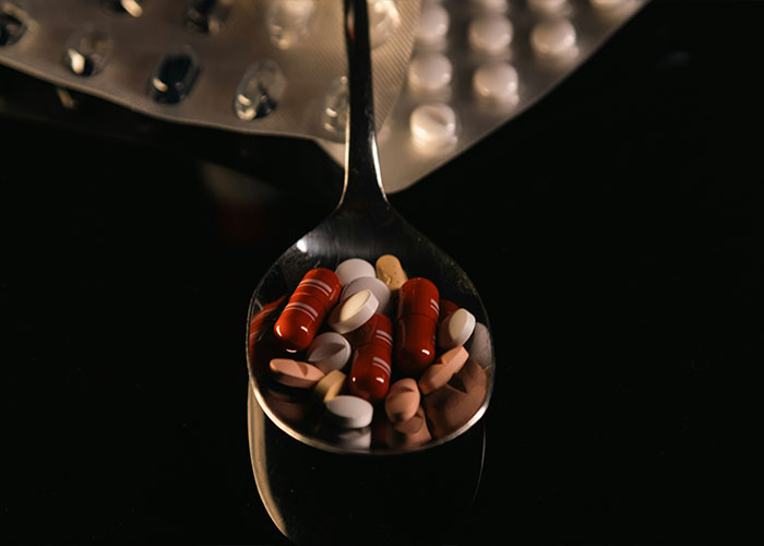 A spoon filled with assorted pills and capsules, representing anti-anxiety medication in a dark setting.