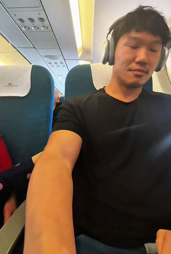 Frequent traveler wearing headphones on an airplane experiencing discomfort from a kid kicking during flight.