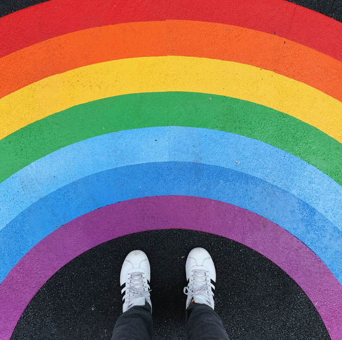 Person wearing white sneakers standing on colorful rainbow pavement, vibrant scene illustrating an Oscar-worthy performance.