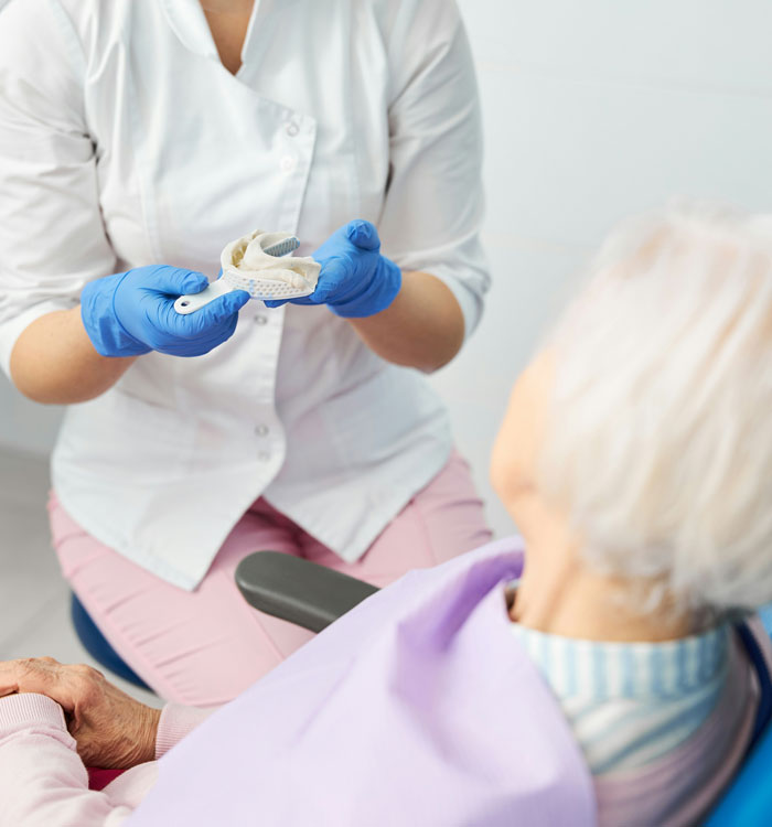 Dentist wearing gloves showing dental mold to elderly patient in clinic, capturing funny patients’ comments atmosphere.