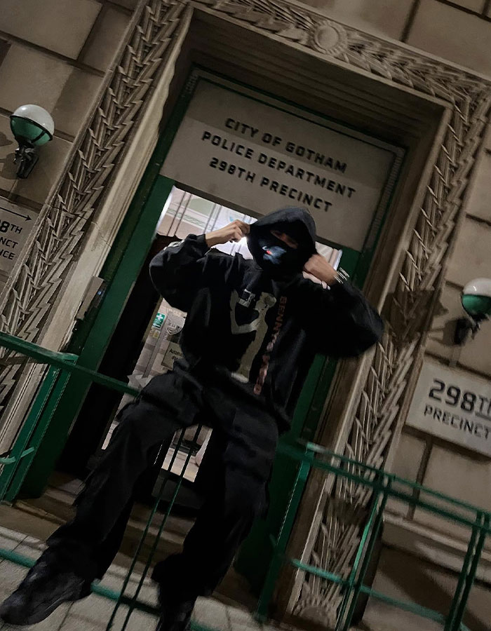 Person in dark hoodie and mask posing outside the City of Gotham Police Department, linked to Timoth&eacute;e Chalamet EsDeeKid theory.