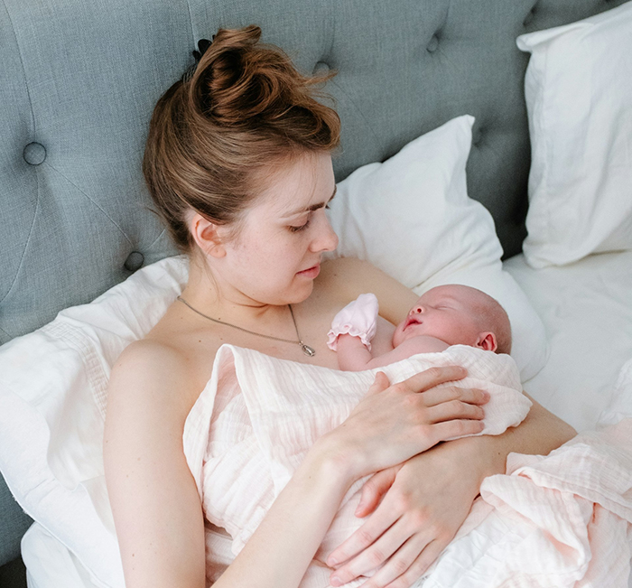 Woman holding newborn baby in bed, reflecting on returning to private office after working from home two years