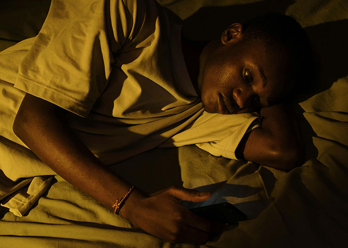 Person lying in bed at night, looking at phone with a worried expression, reflecting terrifying things found online.