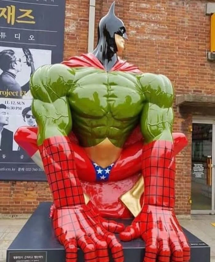 Statue blending Batman, Hulk, Spider-Man, and Captain America features exaggerated muscles in an outdoor urban art display.