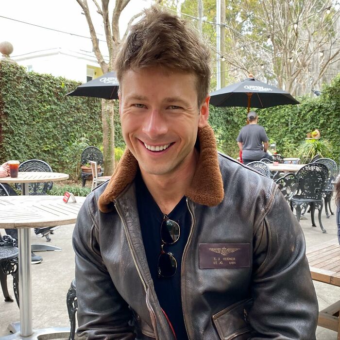 Smiling man in a brown leather jacket outdoors, linked to Glen Powell's viral blunder and dark side of Hollywood discussion.