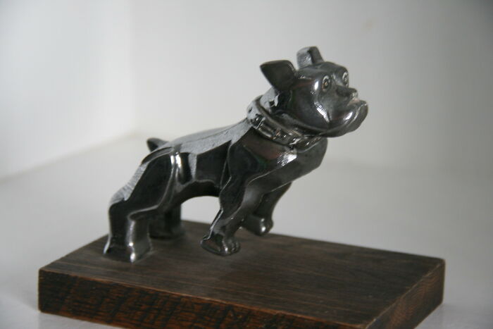 Black metal dog sculpture on a wooden base, resembling a haunting figure truckers might see on the road at night.