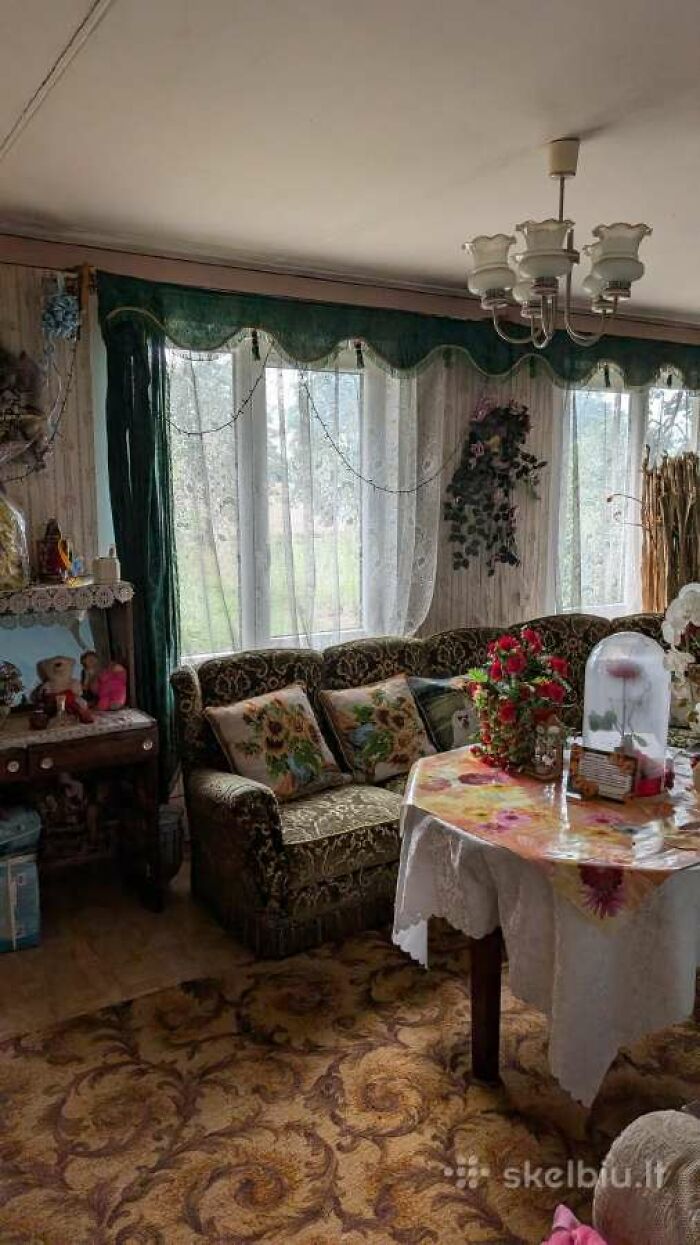 Sala de estar retro con sofá, cortinas, mesas y decoración floral en listado de bienes raíces entretenido y único.