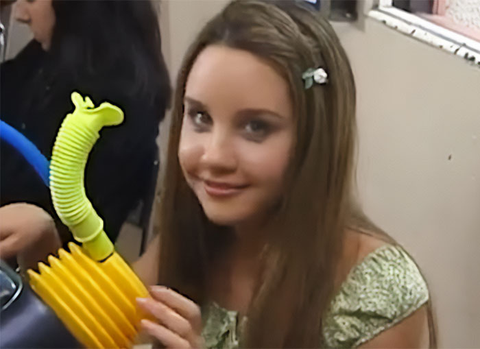 Amanda Bynes smiling indoors holding a yellow and green toy, related to viral claim involving Dan Schneider.