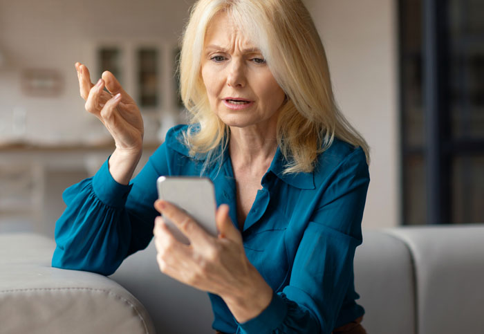 Frustrated middle-aged woman upset while looking at smartphone, illustrating MIL choosing wife and baby over her conflict.