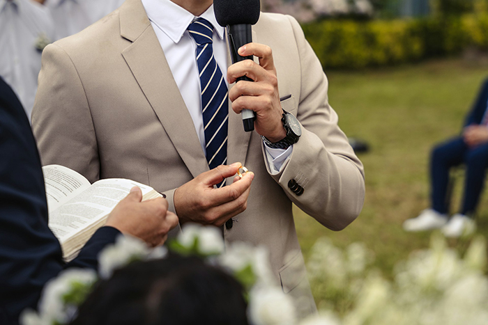 Groom holding wedding ring and microphone during outdoor ceremony, symbolizing vows written with ChatGPT.