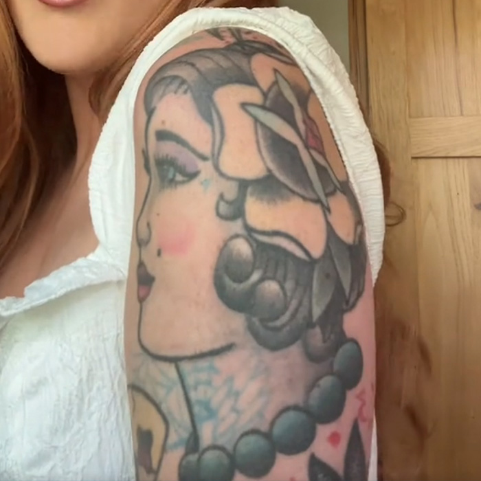 Tattoo artist showing regret with detailed traditional tattoo on upper arm featuring a woman's profile and beads.