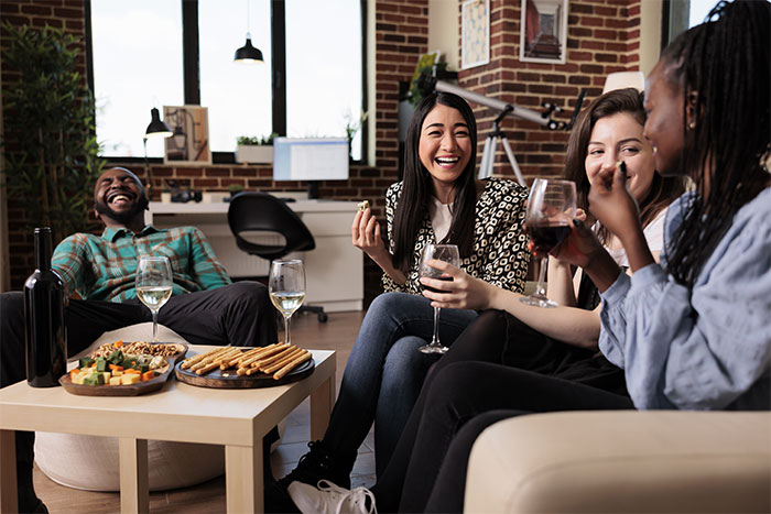 Group of friends socializing and laughing indoors with wine and snacks, capturing a moment of casual fun and connection.