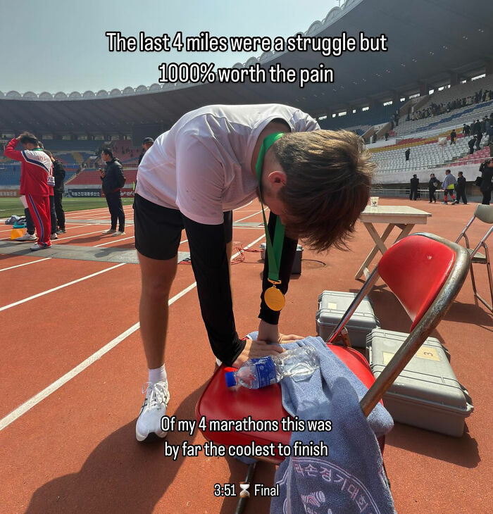 American travel influencer resting after marathon in North Korea, wearing medal and catching breath on the track field.