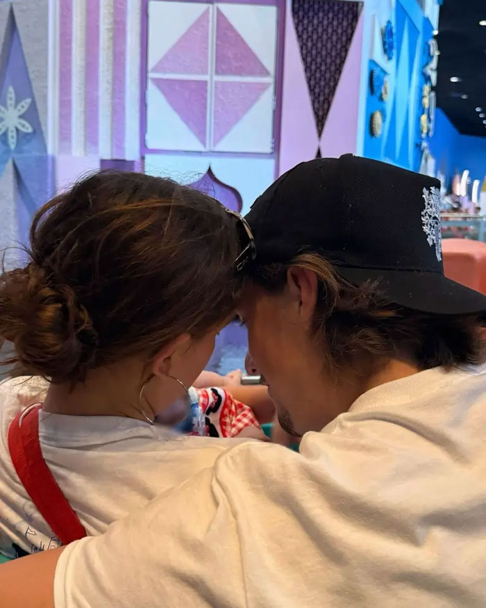 Millie Bobby Brown seen from behind, sharing a close moment in a colorful indoor setting, related to adopting a baby at 21. Millie Bobby Brown seen from behind, sharing a close moment in a colorful indoor setting, related to adopting a baby at 21.