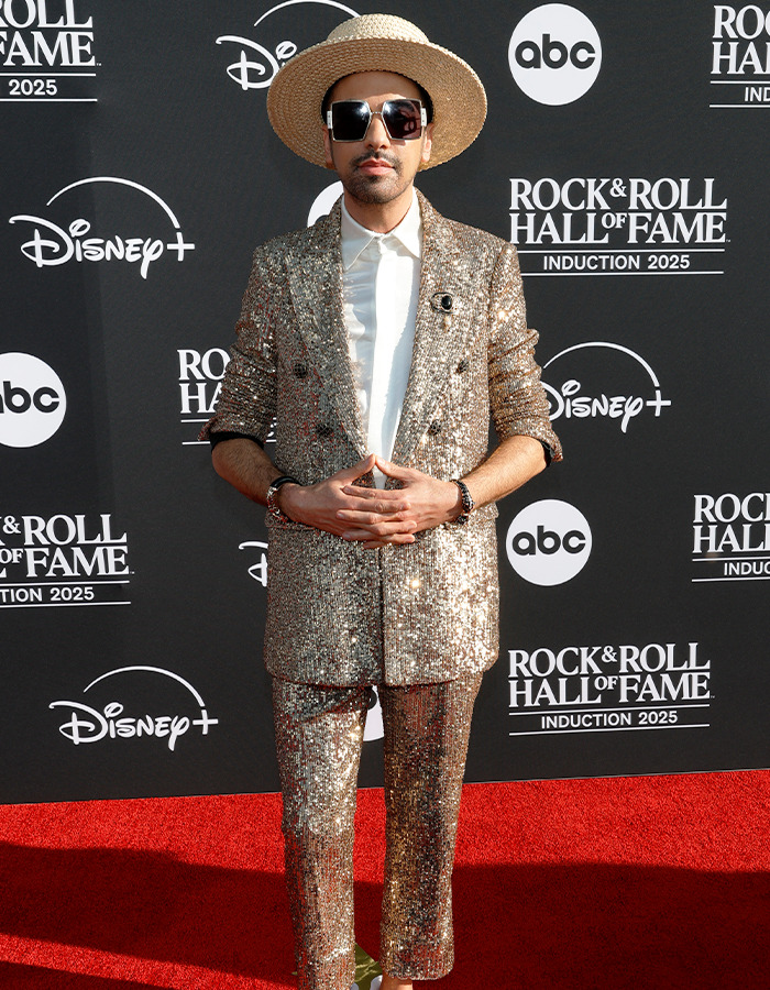 Man in a sparkly gold suit and hat posing on the red carpet at the Rock Hall of Fame 2025 event.