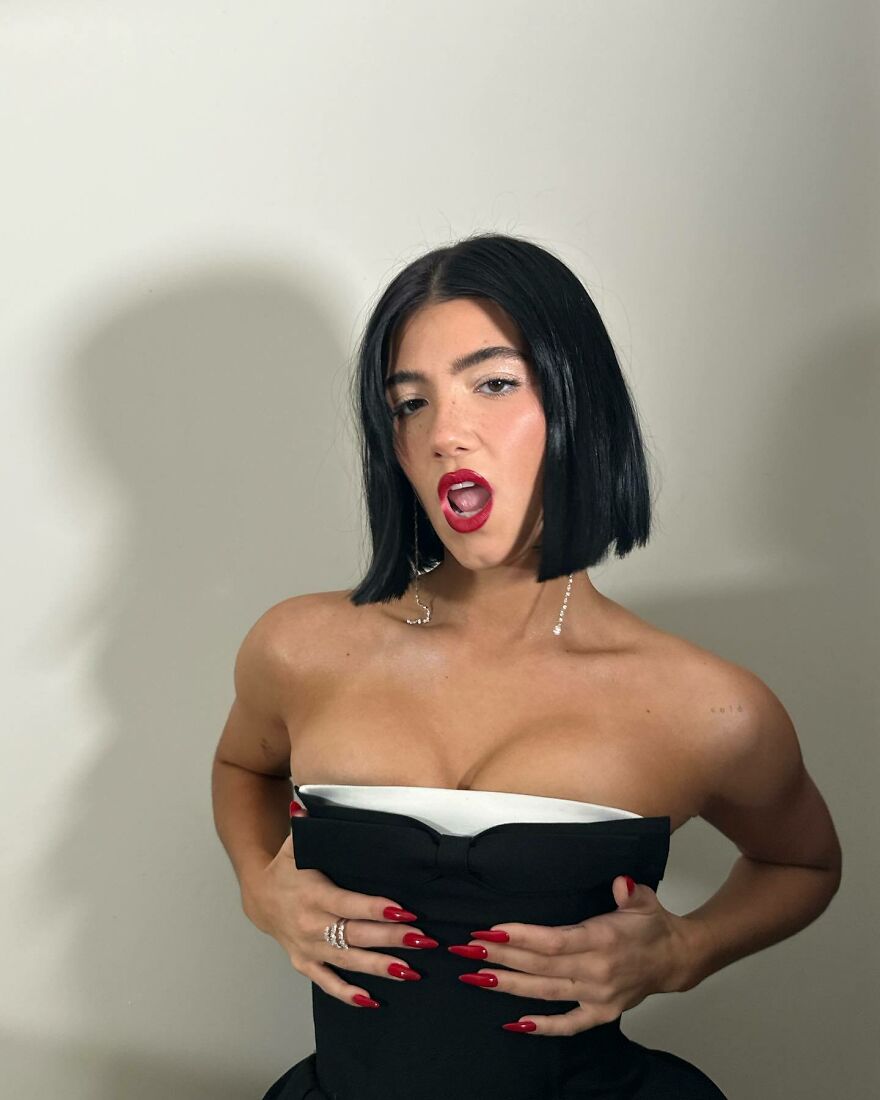 Charli D&rsquo;amelio with short black hair and red lipstick posing in a strapless black dress showcasing teen queen of cash style.