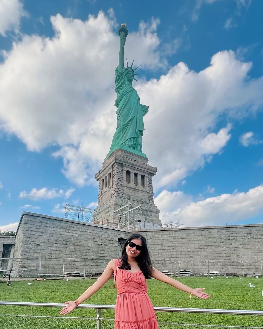 Asian woman smiling and posing near the Statue of Liberty, challenging outdated Asian stereotypes in a modern world.