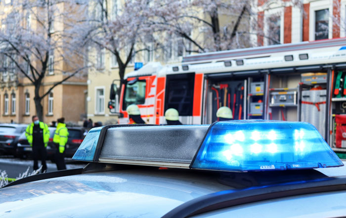 Police car with flashing blue lights in front of firefighters and emergency responders at a city scene of a staged lie.