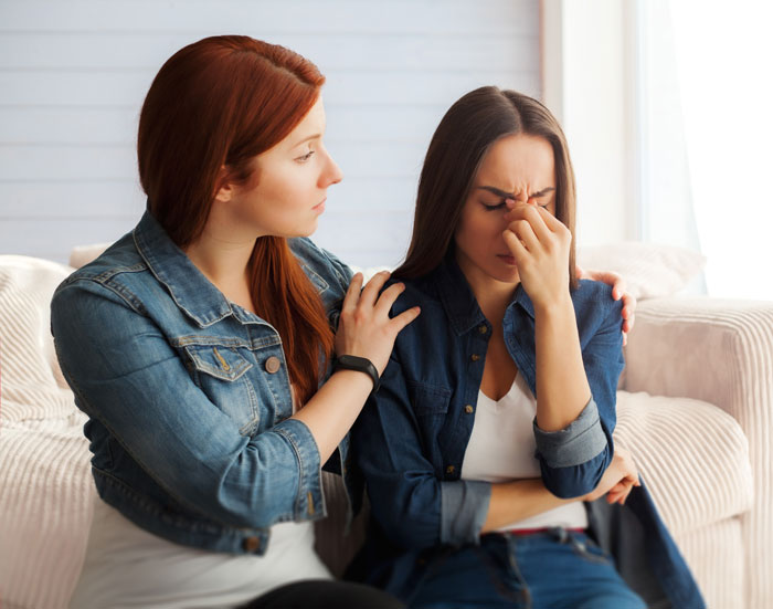Two women sitting on a couch, one comforting the other, representing important girl code rules and support.