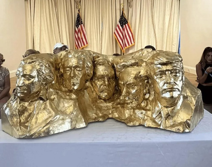 Golden sculpture of five US presidents with American flags in the background, symbolizing Kristi Noem transformation. Golden sculpture of five US presidents with American flags in the background, symbolizing Kristi Noem transformation.